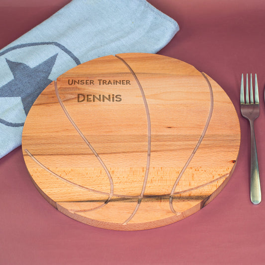 Personalisierbares Holzbrett in Basketballform mit Gravur Unser Trainer Dennis, dekorativ präsentiert