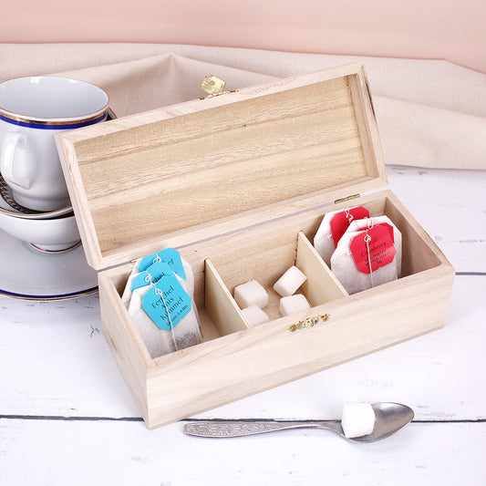 Offene Teebox aus Holz mit drei Fächern, befüllt mit Teebeuteln und Zuckerwürfeln auf hellem Tisch.