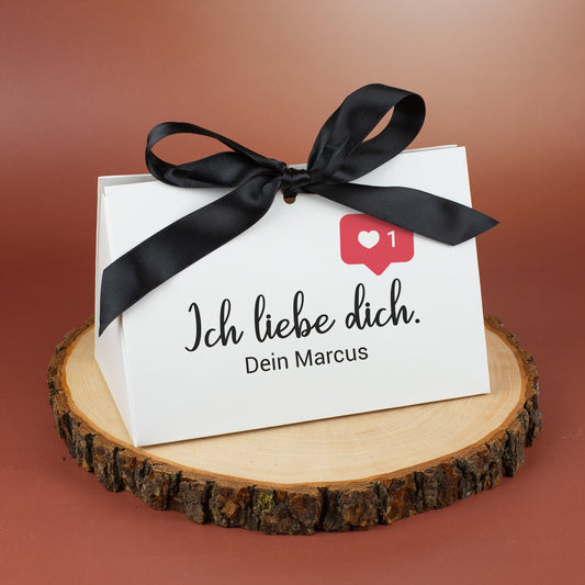 Personalisierte Geschenkverpackung „Ich liebe dich“ mit schwarzer Schleife, Social-Media-Herz-Icon und Wunschtext „Dein Marcus“ auf Holzscheibe