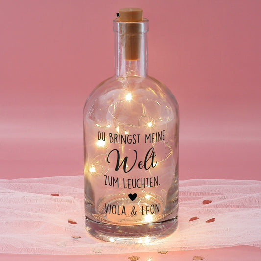 Personalisierte LED-Karaffe aus Glas mit Spruch „Du bringst meine Welt zum Leuchten“ und warmweißer Lichterkette vor rosa Hintergrund