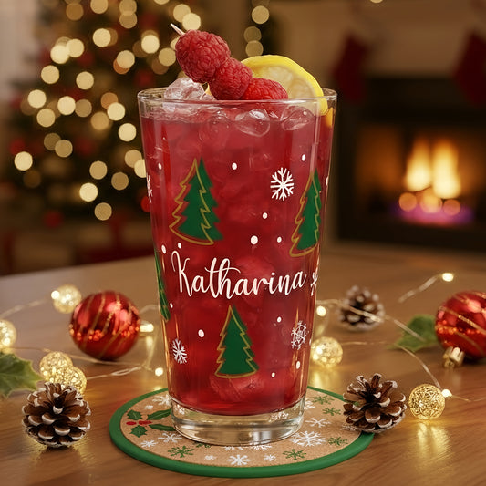 Personalisierbares Weihnachtsglas mit Tannenbaum-Design und Schneeflocken, befüllt mit rotem Getränk und festlich dekoriertem Tisch im Hintergrund.