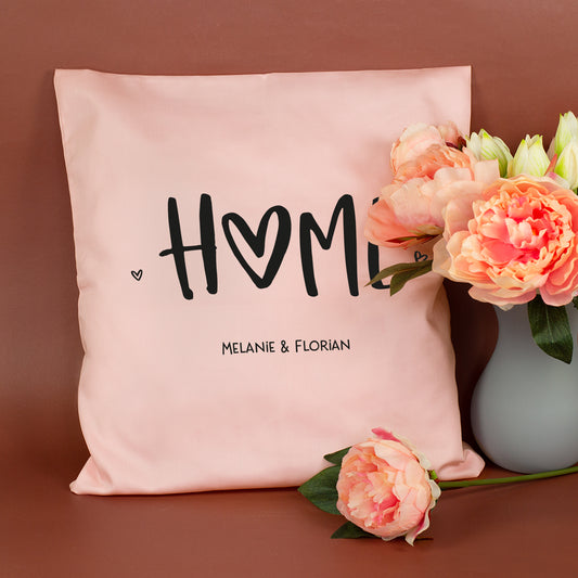 Personalisiertes rosa HOME Kissen mit Wunschtext Melanie und Florian neben Blumen
