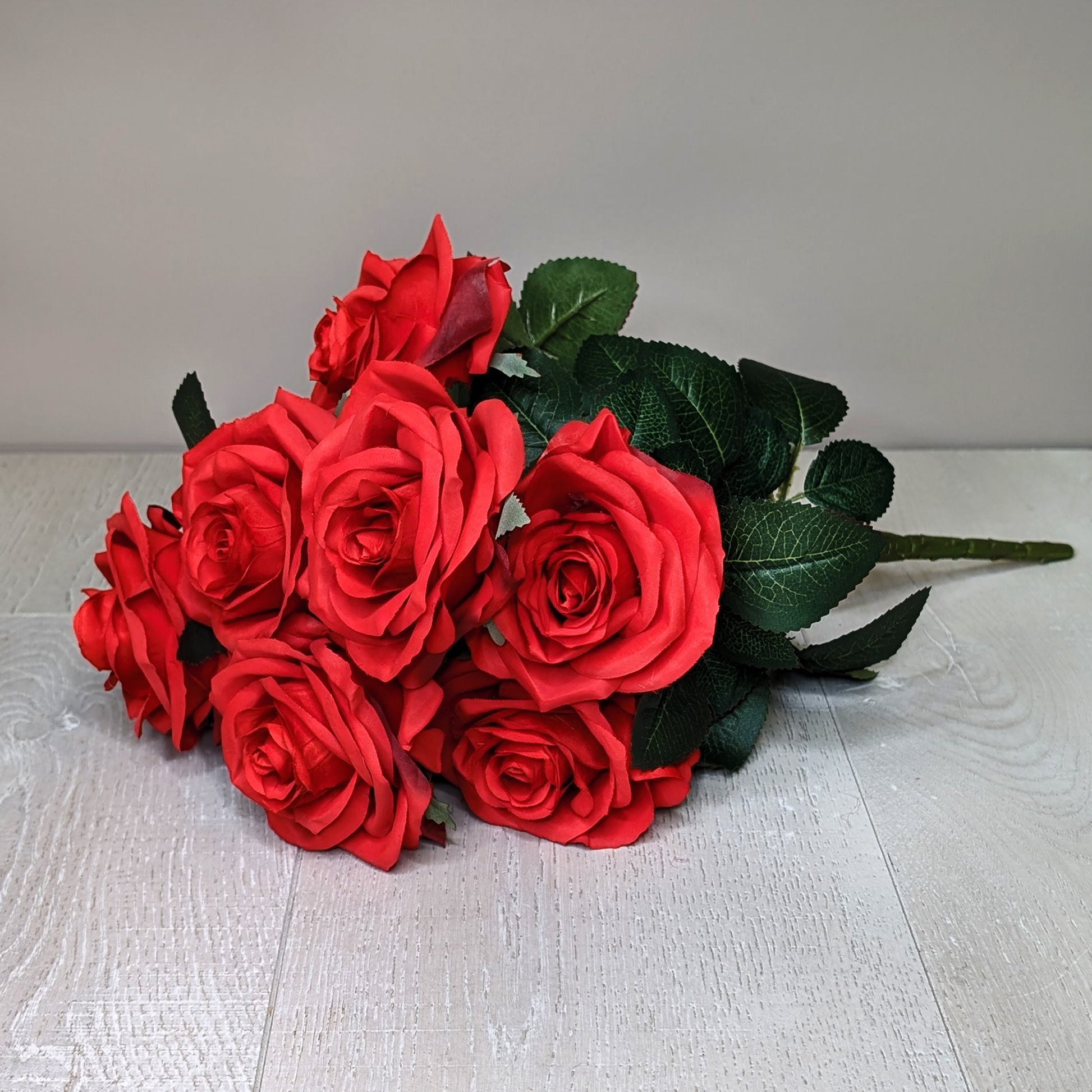 Seidenrosenstrauß in Rot auf hellem Holzboden liegend