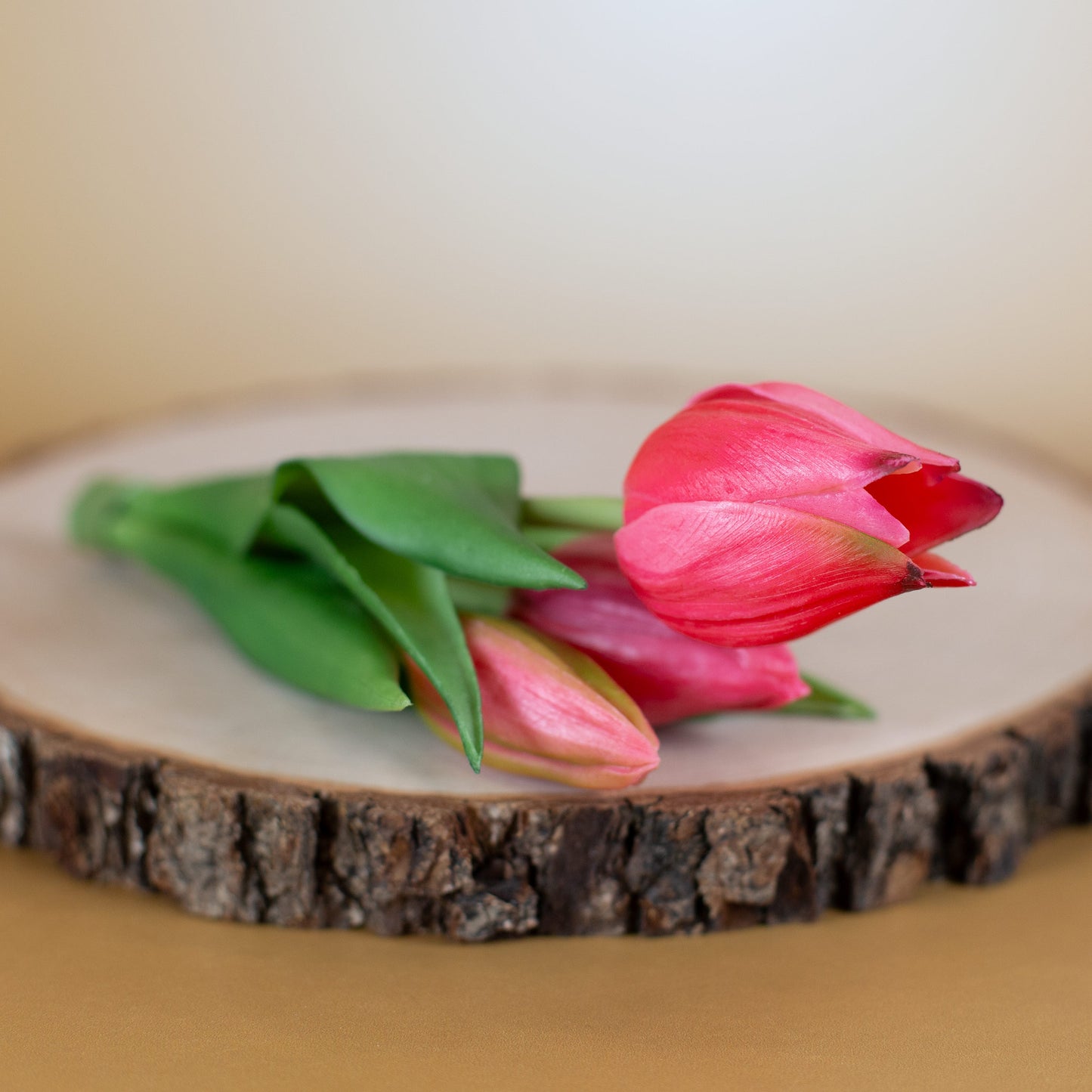 Kunstblumenstrauß aus drei rosa Tulpen liegend auf einer Holzscheibe fotografiert