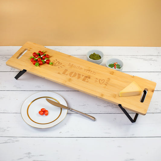 Großes Servierbrett aus zertifiziertem Bambus mit klappbaren Metallfüßen und Made with Love Gravur, angerichtet mit Tomaten, Käse, Dips und Snacks