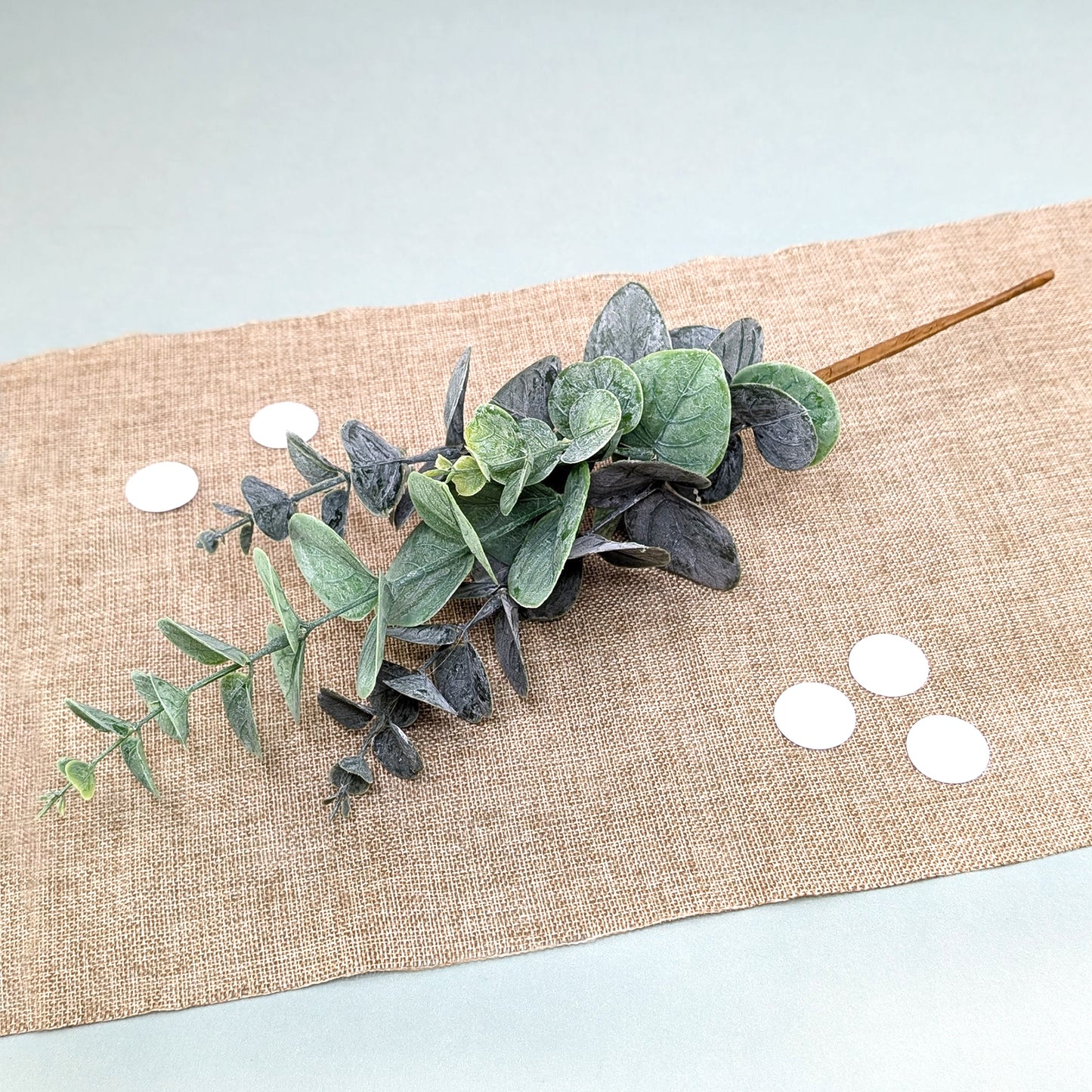 Künstlicher Eukalyptuszweig mit mattgrünen Blättern auf Tischläufer arrangiert