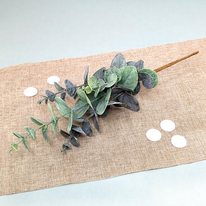 Künstlicher Eukalyptuszweig mit mattgrünen Blättern auf Tischläufer arrangiert