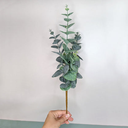 Künstlicher Eukalyptuszweig mit mattgrünen Blättern in Hand gehalten