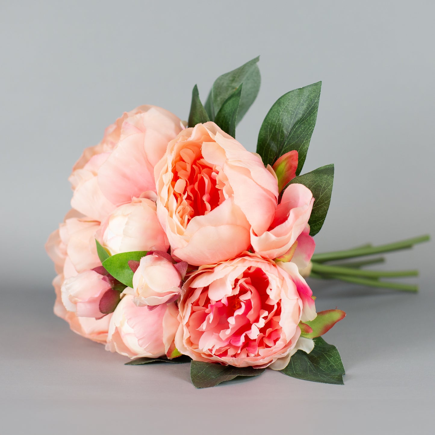 Kunstblumenstrauß mit rosa Pfingstrosen und grünen Blättern – seitlich arrangiert