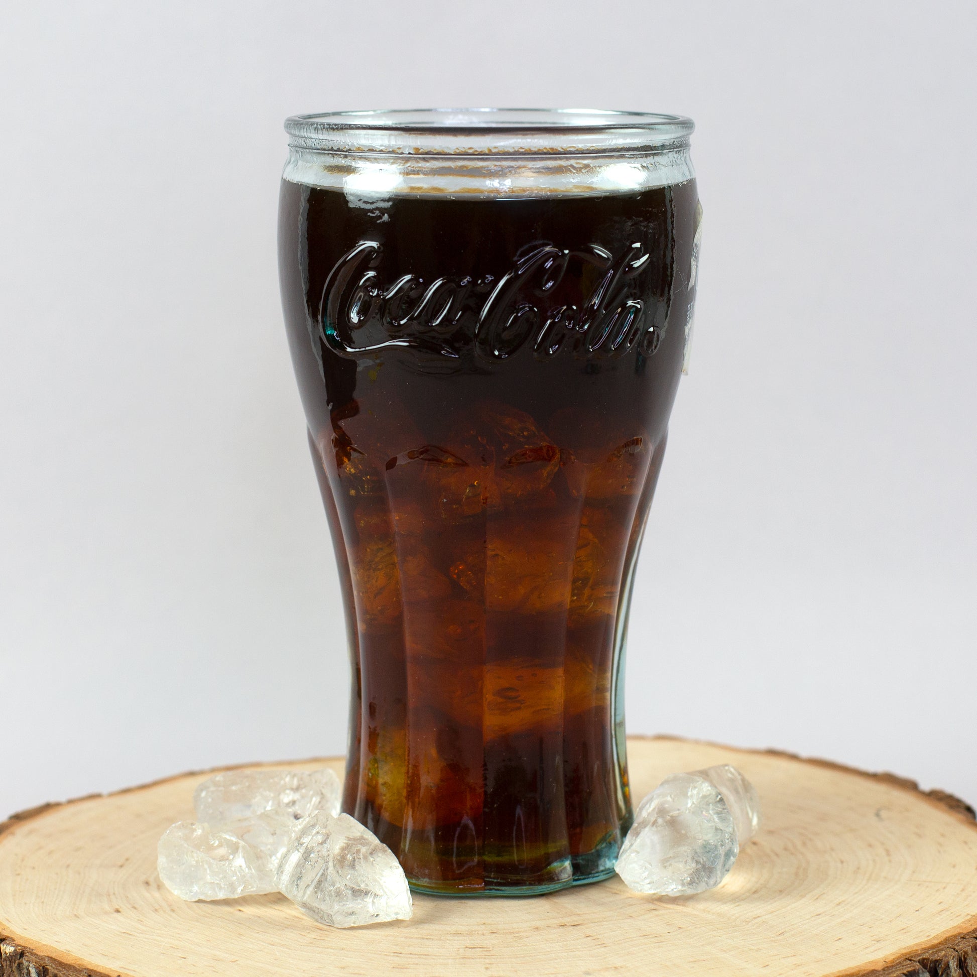 Handgefertigtes Coca-Cola Trinkglas mit Cola und Eiswürfeln auf Holzscheibe