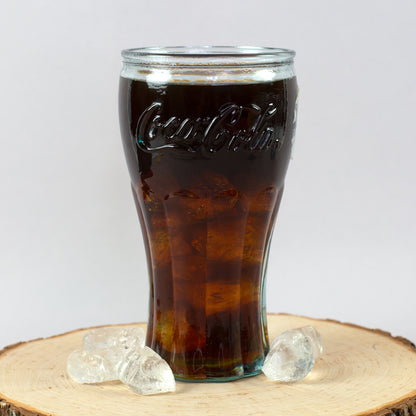 Handgefertigtes Coca-Cola Trinkglas mit Cola und Eiswürfeln auf Holzscheibe