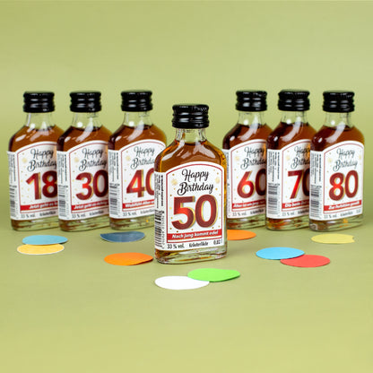 Kräuterlikör-Miniaturen „Happy Birthday“ als Set, vorne Flasche mit rotem Etikett „50 – Nach jung kommt edel“, dahinter weitere Jubiläumszahlen 18 bis 80