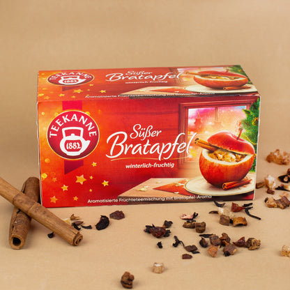 Packung Teekanne Wintertee "Süßer Bratapfel" dekoriert neben Zimtstangen und losem Tee