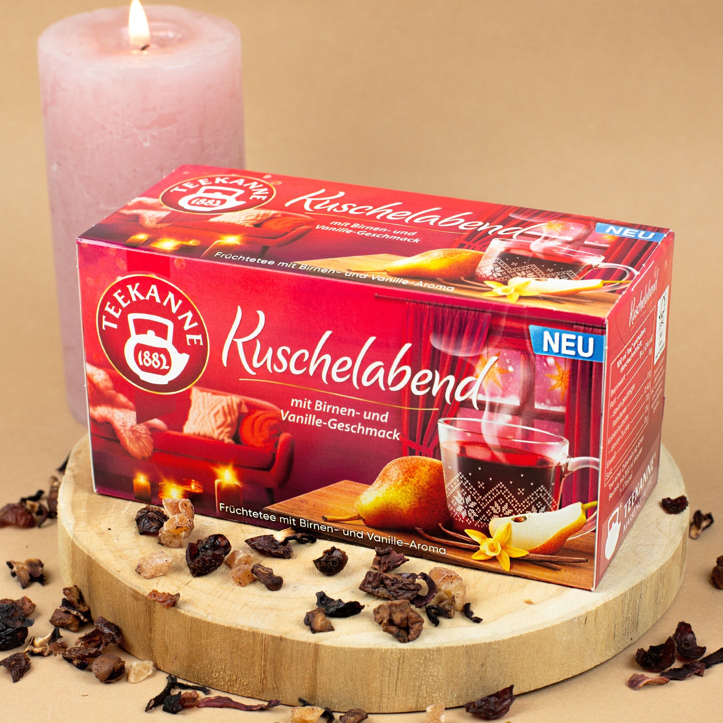 Packung „Teekanne Kuschelabend“ auf Holzscheibe platziert, dekoriert mit losen Teestückchen.