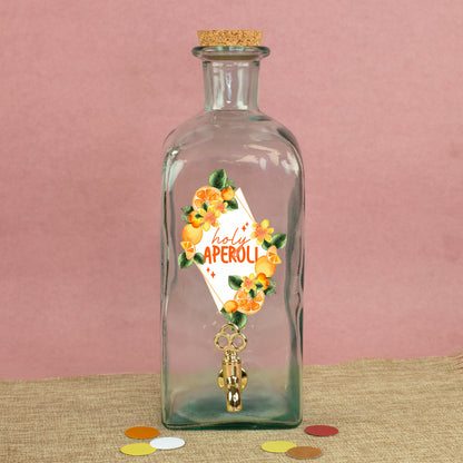 Glas Getränkespender mit Zapfhahn und sommerlichem Orangen-Motiv auf Stoffunterlage vor rosa Hintergrund