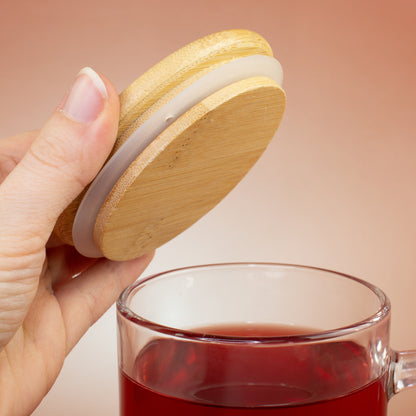 Hand hält den Bambusdeckel mit Dichtungsring über der mit rotem Tee gefüllten Glastasse
