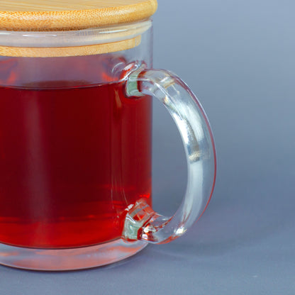 Detailansicht des transparenten Henkels der Glastasse mit rotem Tee und aufgesetztem Bambusdeckel