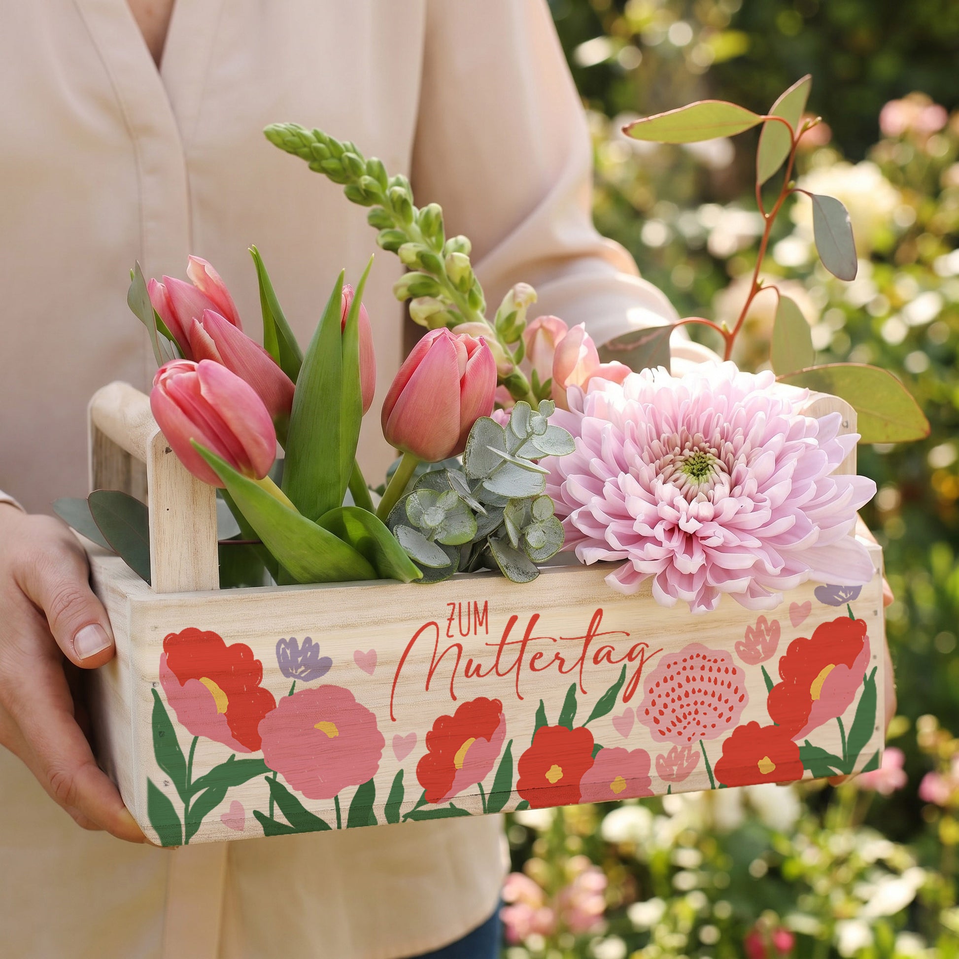 Pflanzkorb aus Holz wird im Garten mit Blumenarrangement zum Muttertag gehalten