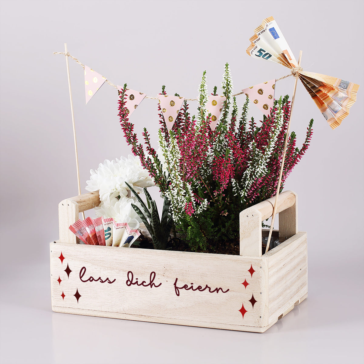 Holzkiste zum Geburtstag mit Heidepflanze, Blumen, Geldscheinen, Wimpelgirlande und Aufdruck „Lass dich feiern“