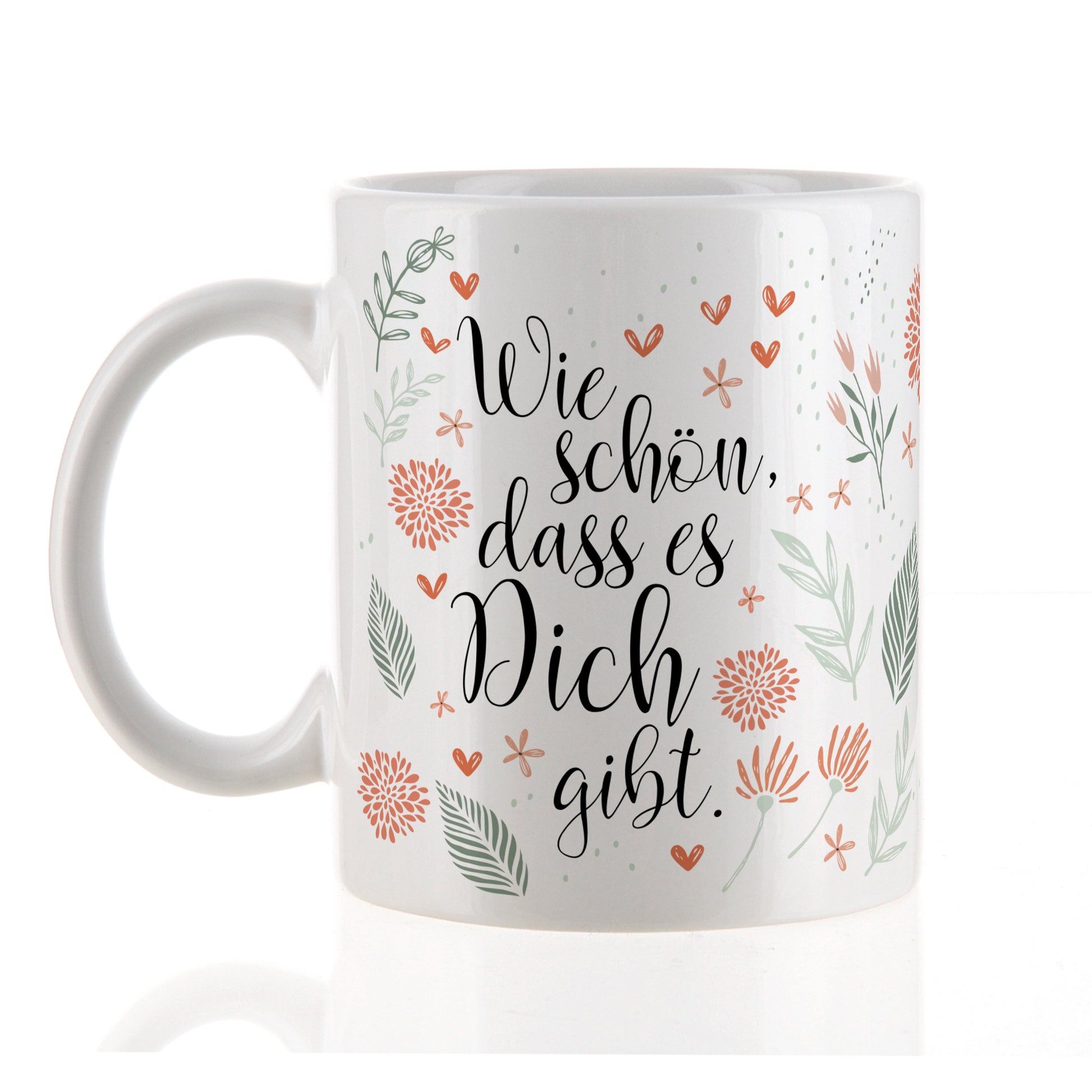 Weiße Keramiktasse mit floralem Dekor und Spruch „Wie schön, dass es Dich gibt“ auf heller Fläche stehend.
