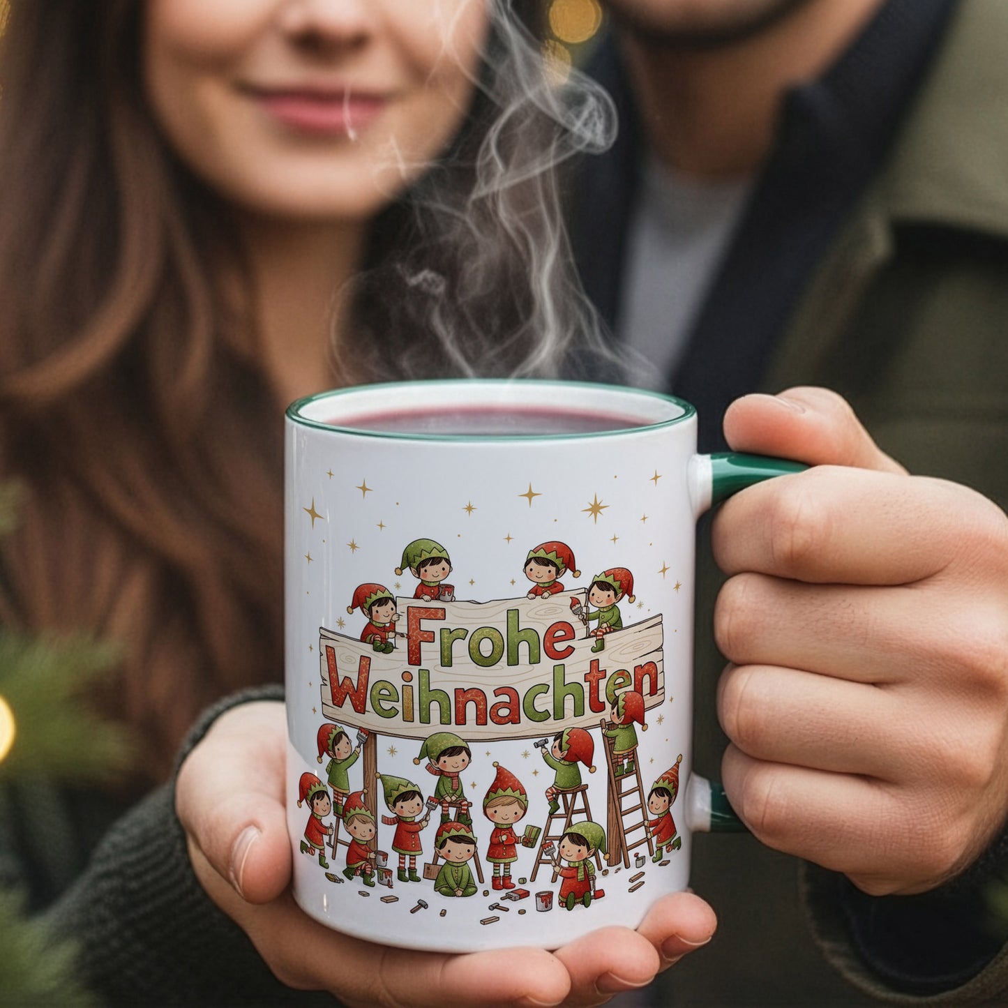 Person hält eine dampfende Weihnachtstasse mit werkelnden Wichteln am „Frohe Weihnachten“-Schild; Paar im Hintergrund leicht unscharf.