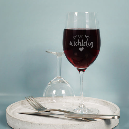 Leonardo-Weinglas aus Teqton-Glas mit Gravur „Du bist mir wichtelig“, Rotwein, dekorativ arrangiert auf hellem Untergrund.