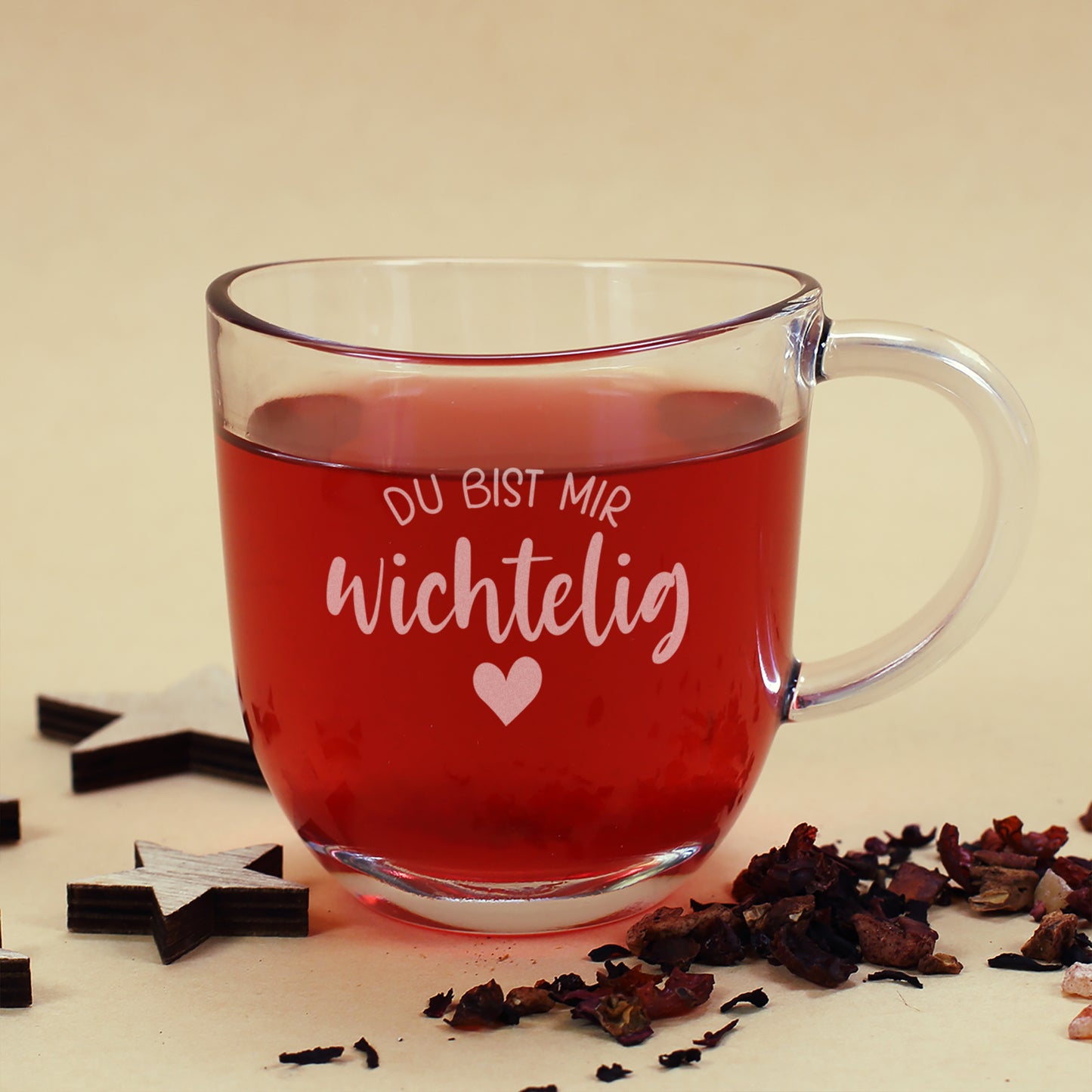 Teeglas mit Gravur „Du bist mir wichtelig“ und Herzmotiv, gefüllt mit Tee, dekoriert mit Holzsternen.