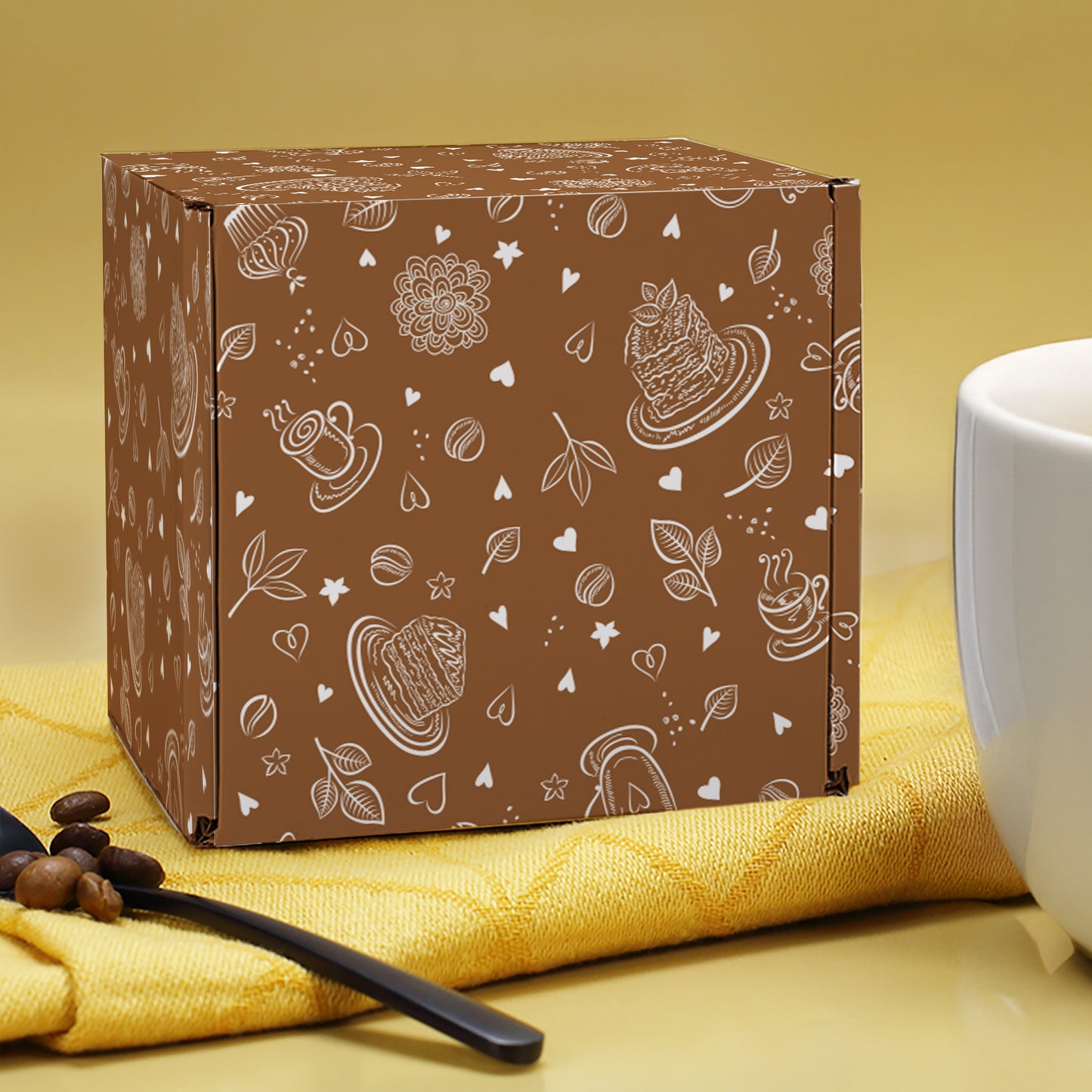 Braune Geschenkbox mit Kaffeebohnen- und Tassenmotiv, liegend neben Löffel, Kaffeebohnen & Tasse.