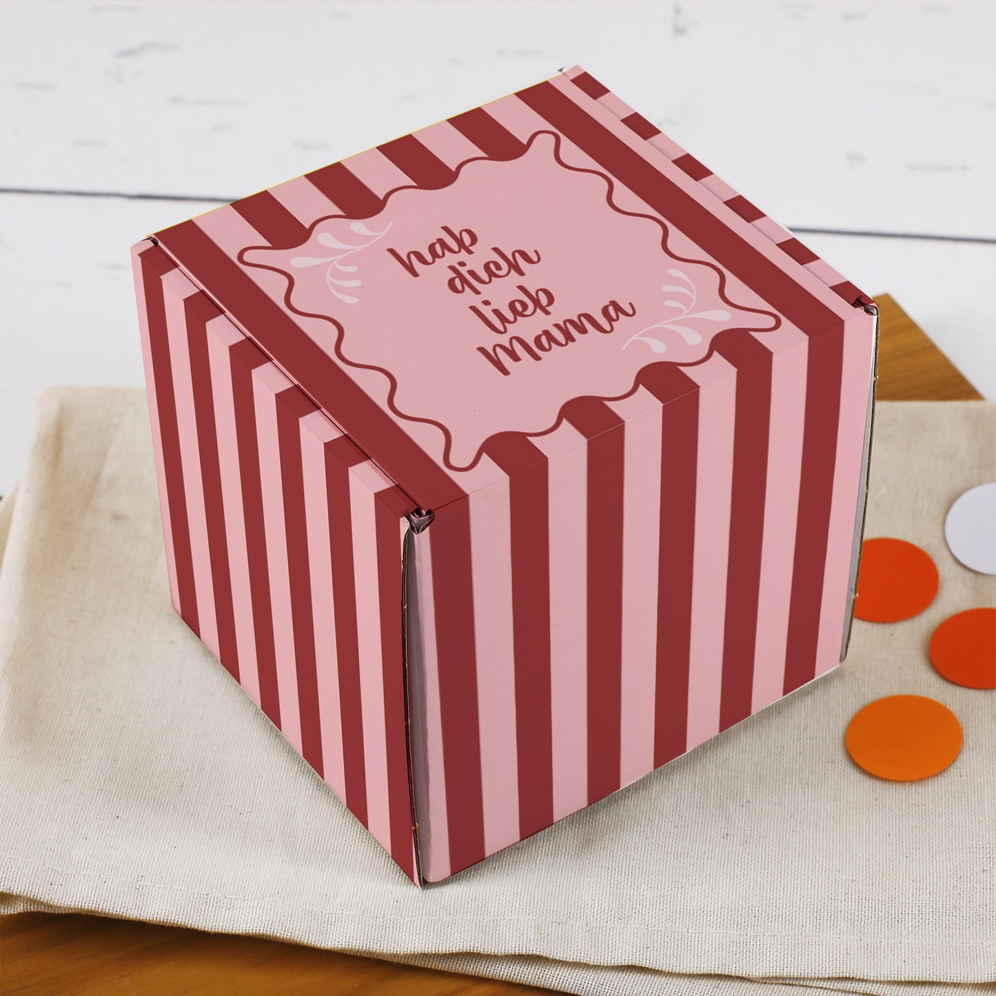 Geschenkbox mit Spruch „hab dich lieb Mama“ in schräger Ansicht auf Stoffunterlage, rosa-rotes Streifenmuster rundum bedruckt