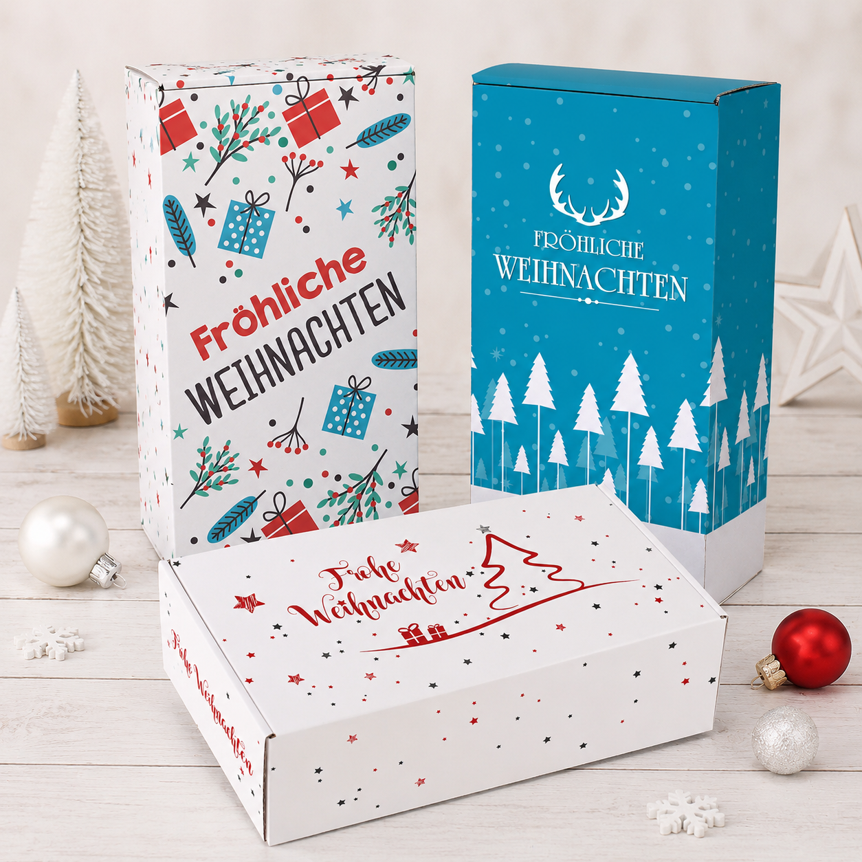 Drei Geschenkboxen zu Weihnachten in verschiedenen Größen mit festlichen Motiven, Fröhliche Weihnachten Aufdruck und winterlicher Deko auf hellem Holzuntergrund