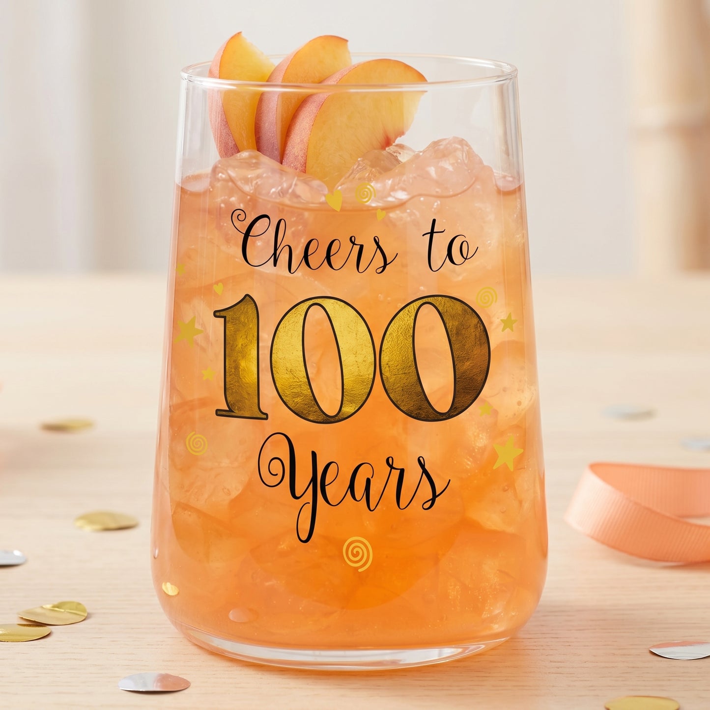 Cocktailglas zum 100. Geburtstag mit orangefarbenem Drink, Eiswürfeln und Pfirsichgarnitur