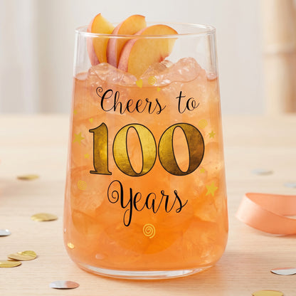 Cocktailglas zum 100. Geburtstag mit orangefarbenem Drink, Eiswürfeln und Pfirsichgarnitur