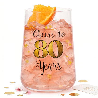 Geschenkglas zum 80. Geburtstag mit rosa Getränk, Eiswürfeln und Orangenscheibe auf heller Dekoration