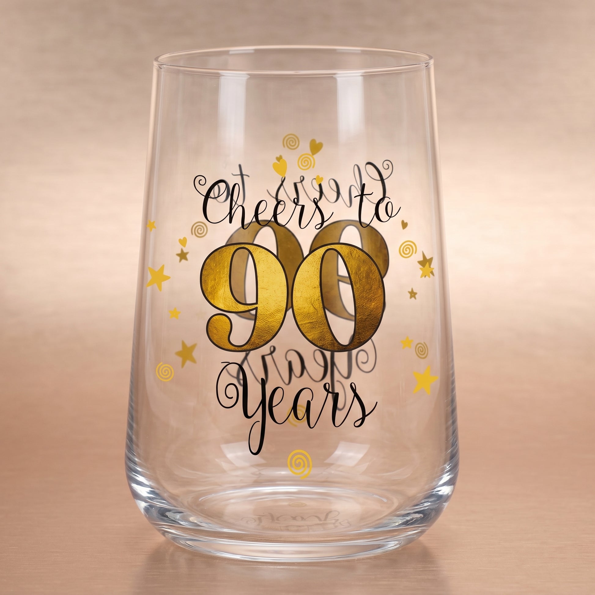Leeres Trinkglas zum 90. Geburtstag mit goldfarbener 90 und „Cheers to 90 Years“-Aufdruck auf Holzuntergrund
