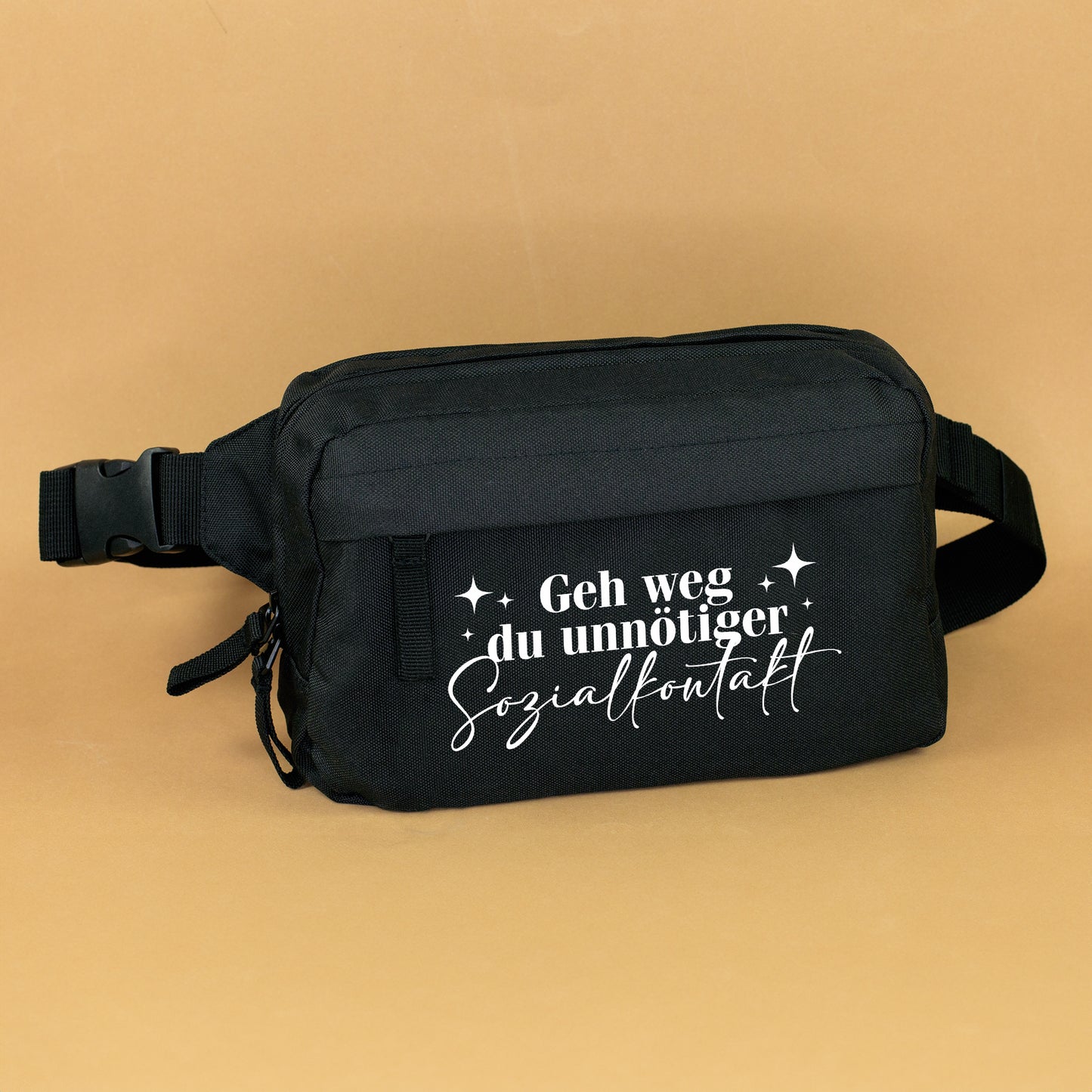Schwarze Bauchtasche mit weißem Spruch „Geh weg du unnötiger Sozialkontakt“ auf warmem Hintergrund