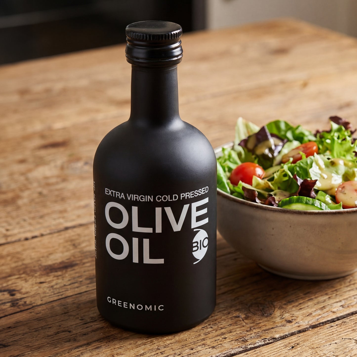 Schwarzes Olivenöl nativ extra in edler Flasche neben Salatschüssel auf Holztisch