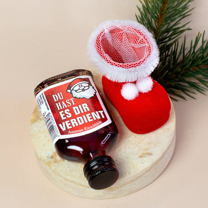 Szene mit liegender Likörflasche „Du hast es dir verdient“ neben leerem Nikolausstiefel. Der Likör ist seitlich positioniert, der Stiefel steht leicht angewinkelt auf heller Steinplatte.
