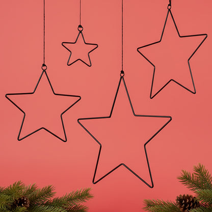 Vier schwarze Metallsterne in verschiedenen Größen hängen dekorativ vor rotem Hintergrund. Im unteren Bereich sind grüne Tannenzweige mit Zapfen zu sehen.