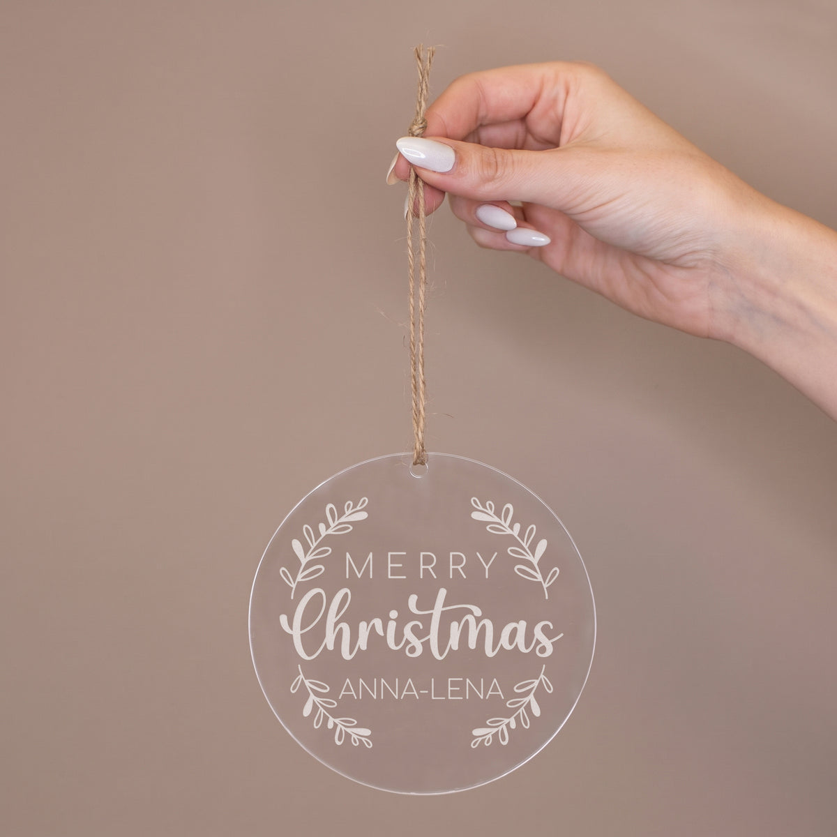 Hand hält runde Acryl Weihnachtsbaumkugel mit Juteband, „Merry Christmas“ Motiv und personalisiertem Namen Anna-Lena