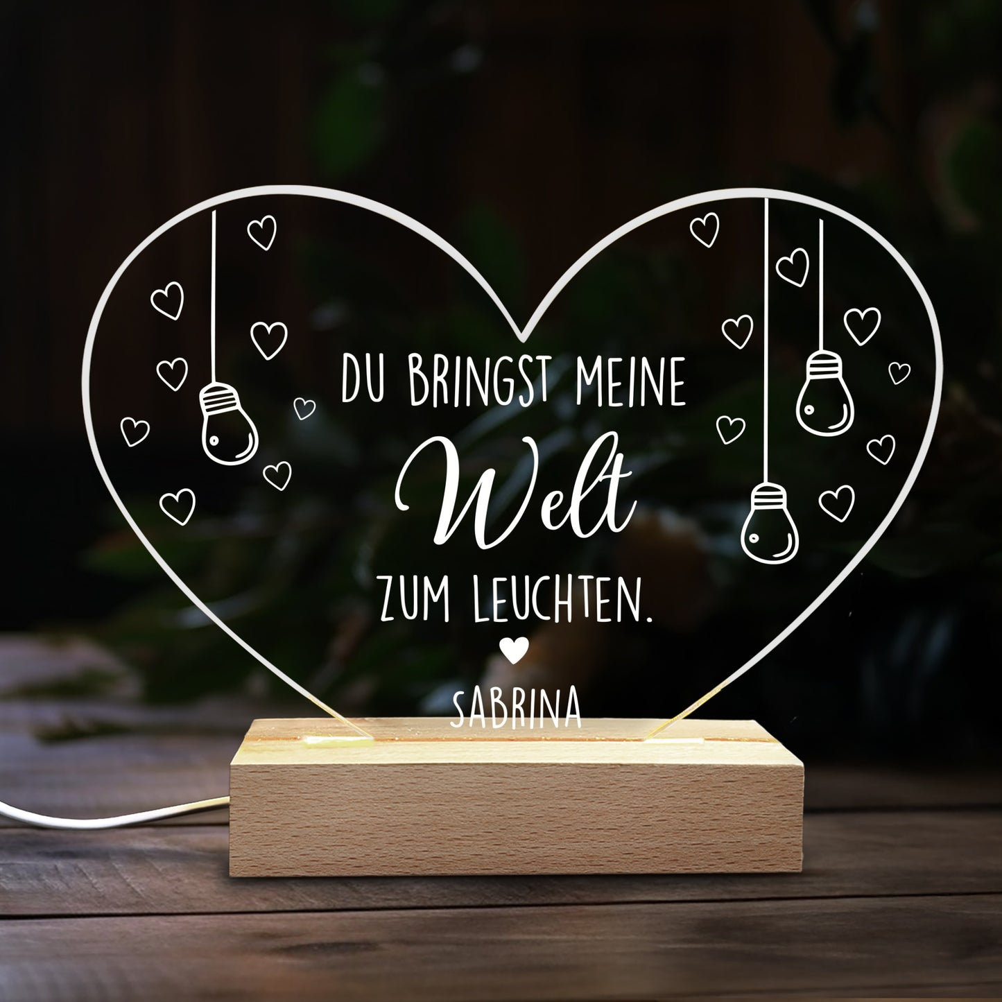Herzförmige LED Acryl-Lampe mit Spruch „Du bringst meine Welt zum Leuchten“ und Name „Sabrina“ vor dunklem Hintergrund