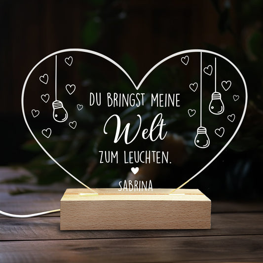 Herzförmige LED Acryl-Lampe mit Spruch „Du bringst meine Welt zum Leuchten“ und Name „Sabrina“ vor dunklem Hintergrund