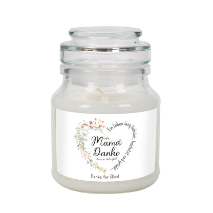 Duftkerze im Glas mit Deckel, stehend vor weißem Hintergrund. Das Etikett trägt ein liebevoll gestaltetes Wiesenblumen-Herz, das den Spruch „Ein Leben lang behütet, beschützt und geliebt…“ umrahmt. In der Mitte steht „Liebe Mama, Danke, dass es dich gibt!“. Die personalisierbare Textzeile unten zeigt „Danke für Alles!“. Perfektes Geschenk zum Muttertag oder Geburtstag, mit einer warmen, persönlichen Botschaft.
