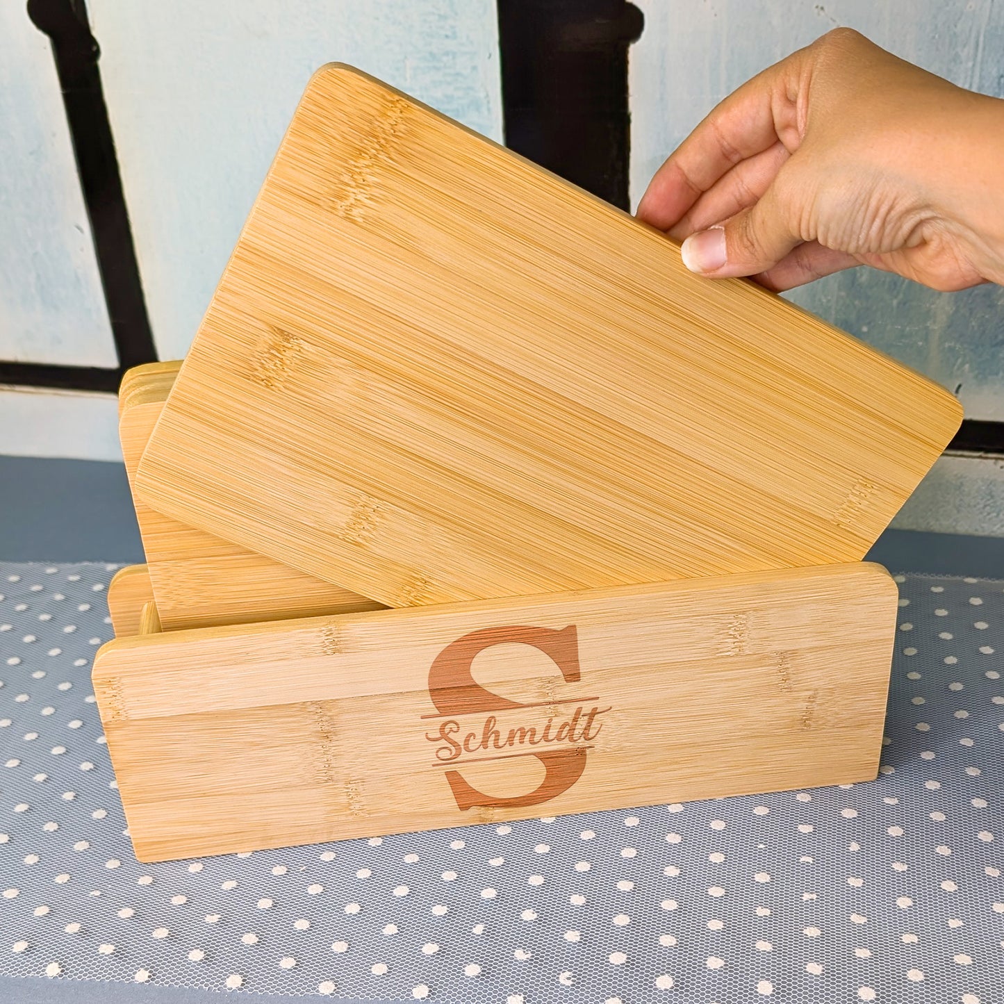 Person entnimmt ein Bambusbrettchen aus einem gravierten Brettchenständer mit dem Motiv „S Schmidt“.