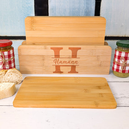 Brettchenständer mit fünf Bambusbrettchen, graviert mit dem Buchstaben „H“ und Namen „Hamann“, dazu Brot und Gläser mit Brotaufstrich.