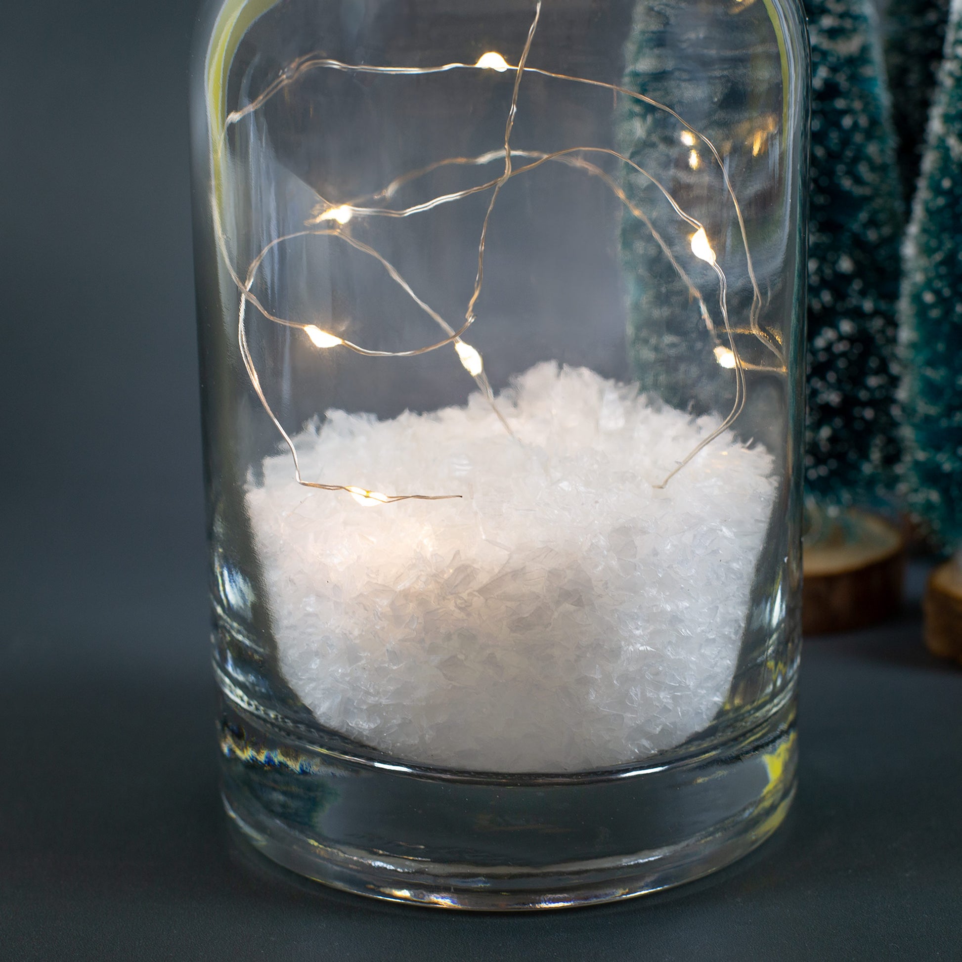 Detailaufnahme von Kunstschnee und LED-Lichterkette im Inneren der Glasflasche.