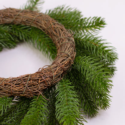 Künstlicher Tannenkranz mit braunem Zweiggeflecht auf weißem Hintergrund