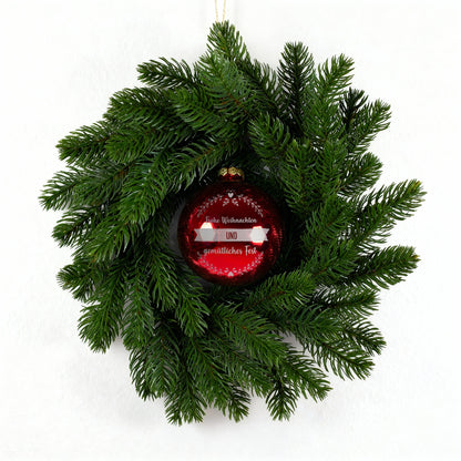 Kunst-Tannenkranz mit roter gravierter Weihnachtskugel vor hellem Hintergrund