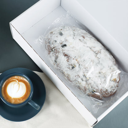 Rosinenstollen in geöffneter weißer Geschenkbox neben einer Tasse Kaffee als Weihnachtsgeschenk