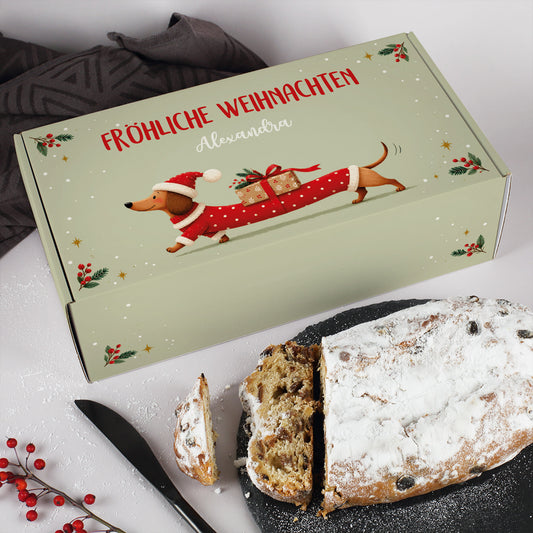 Personalisierte Stollen Geschenkbox mit Dackel in Weihnachtskleidung neben angeschnittenem Rosinenstollen
