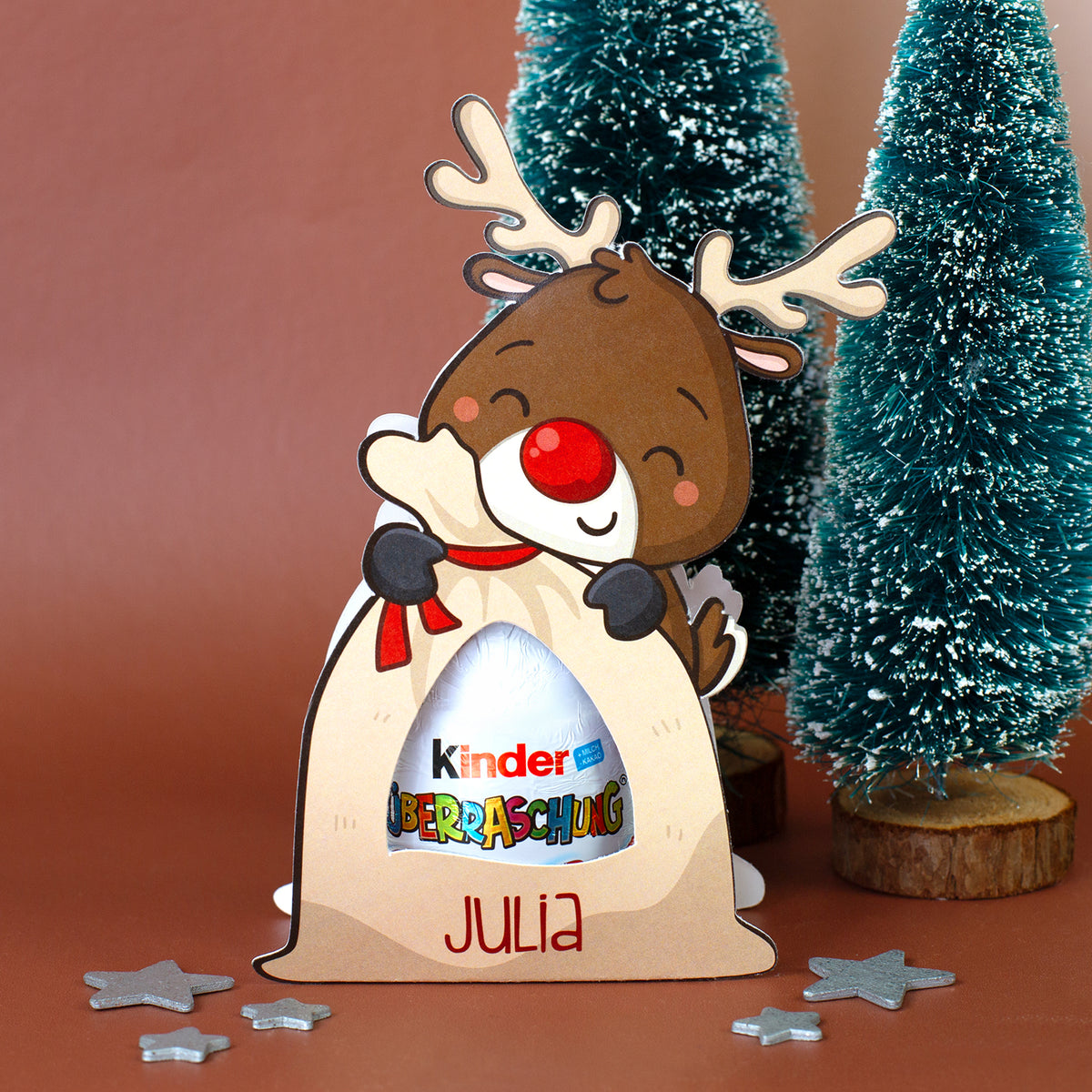 Rentier-Geschenkverpackung mit Kinder Überraschung und Name Julia vor weihnachtlichen Mini-Tannenbäumen